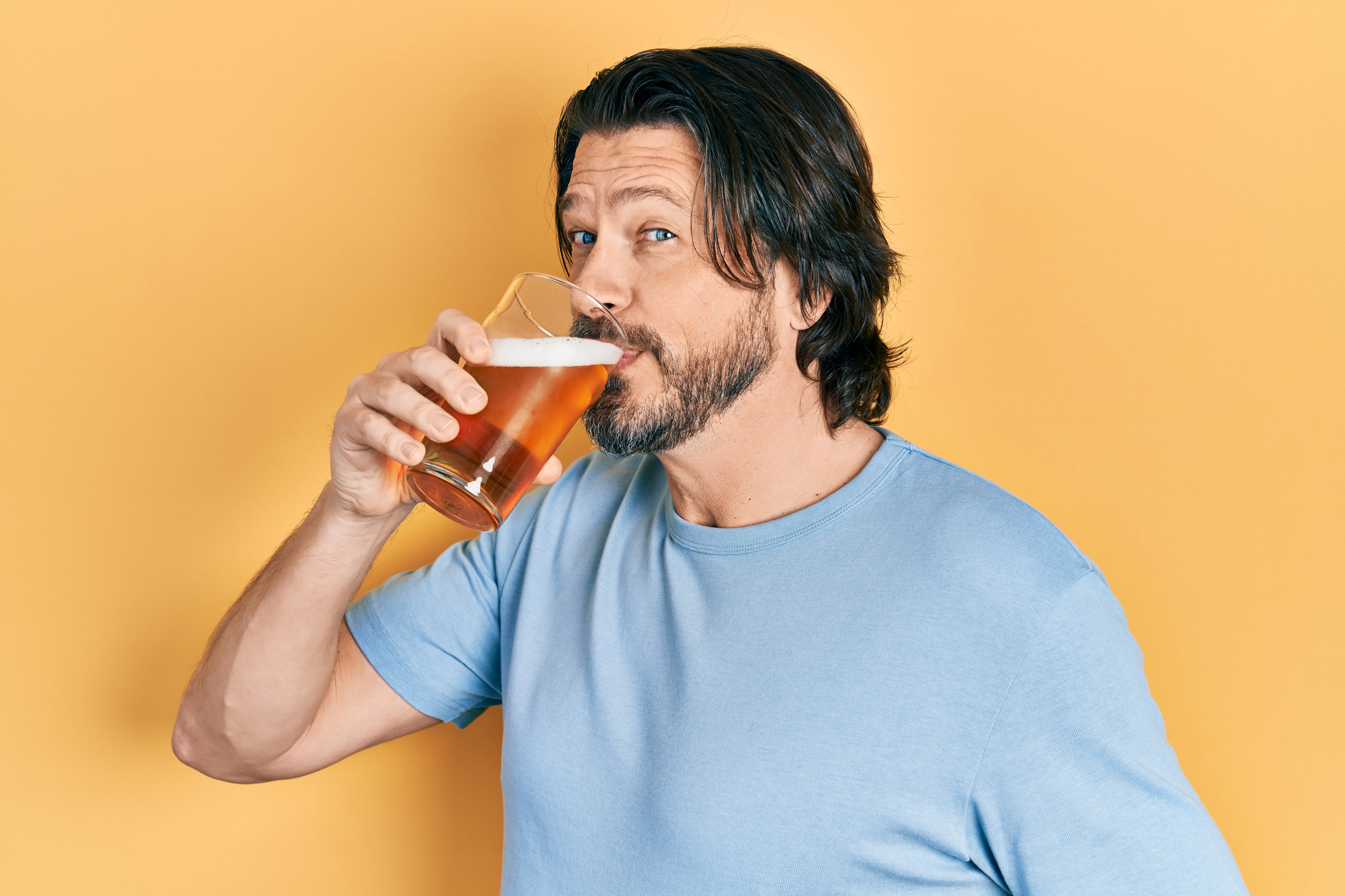 Middle age caucasian man with beard drinking a pint glass of fresh beer
