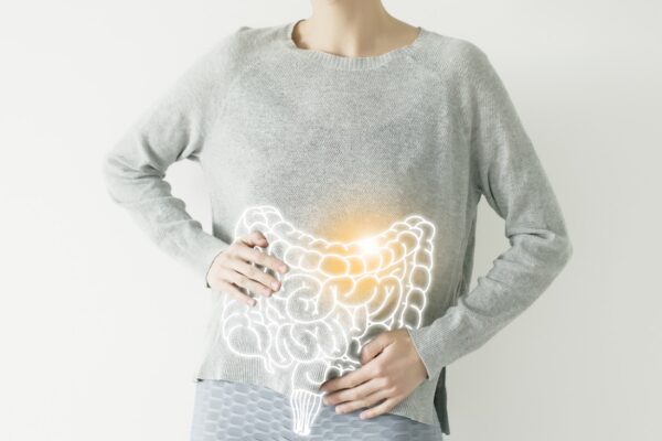Person wearing gray sweater with illuminated digestive system overlay, hands placed on stomach area, representing gut health awareness and healing