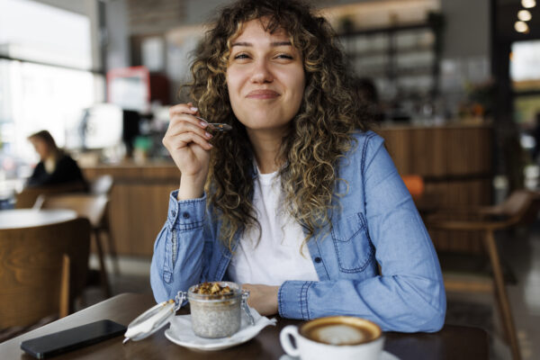 Smiling young woman eating chia pudding for breakfast at cafe